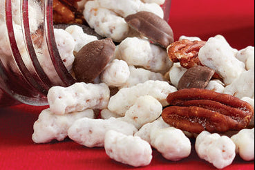 A clear glass jar tipped on its side with white popcorn-like snack pieces and brown pecans spilling out onto a bright red background.